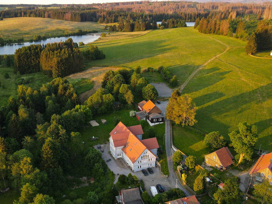 Harz-Urlaubs-Alm in Buntenbock - Hotel, Wiesen und Teich aus der Luft Die Luftaufnahme zeigt das idyllisch gelegene Hotel Urlaubs-Alm Buntenbock im Harz, umgeben von saftigem Grün und einem Teich. Ein perfekter Rückzugsort inmitten der Natur.