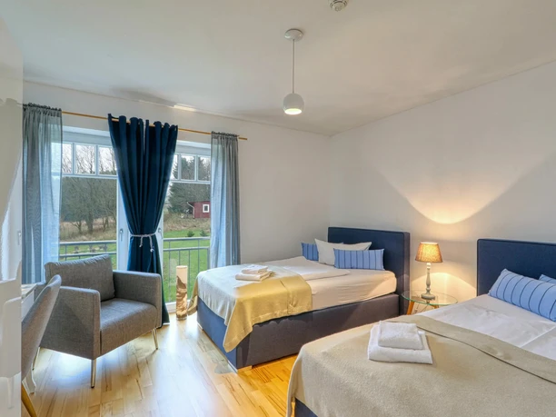 Ein freundlich gestaltetes Zimmer in der Harz-Urlaub-Alm mit zwei Einzelbetten, Lampen, Sessel und Ausblick in einen Garten.