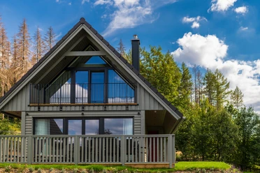 Gemütliches Ferienhaus in der Harz-Urlaubs-Alm mit großer Fensterfront, eingebettet in Bäume unter blauem Himmel.