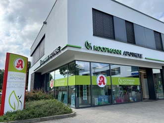 Koopmann Apotheke.jpg Die Koopmann Apotheke ist ein modernes Gebäude mit großer Glasfassade und hellen Schildern.