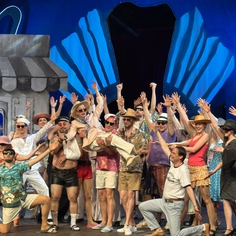 IMG_6384.JPEG Gruppe von Darstellerinnen und Darstellern in farbenfrohen Sommerkostümen auf einer Theaterbühne
