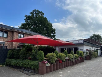 Bild1.jpg Vor einem Restaurant mit dem Banner "Da Mama" stehen rote Sonnenschirme über einer Terrasse mit grünen Pflanzen.
