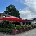 Bild1.jpg Vor einem Restaurant mit dem Banner "Da Mama" stehen rote Sonnenschirme über einer Terrasse mit grünen Pflanzen.
