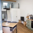 Helle Ferienwohnung mit offenem Wohnbereich, moderner Küche, Esstisch und einer Treppe zur Galerie.