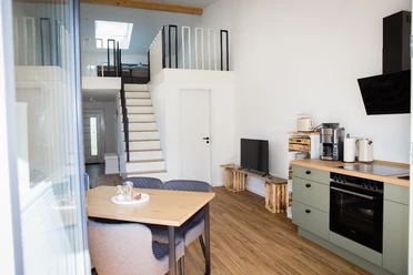 Bröcklingshof_Fewo (15).jpg Helle Ferienwohnung mit offenem Wohnbereich, moderner Küche, Esstisch und einer Treppe zur Galerie.