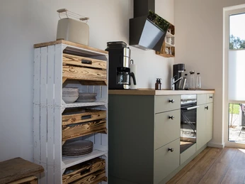 Moderne Küche mit Holzregalen, Kochfeld, Ofen, Kaffeemaschine und Zugang zu einem Sonnenfenster.