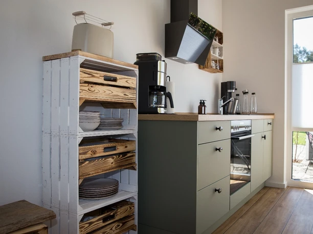 Bröcklingshof_Fewo (18).jpg Moderne Küche mit Holzregalen, Kochfeld, Ofen, Kaffeemaschine und Zugang zu einem Sonnenfenster.