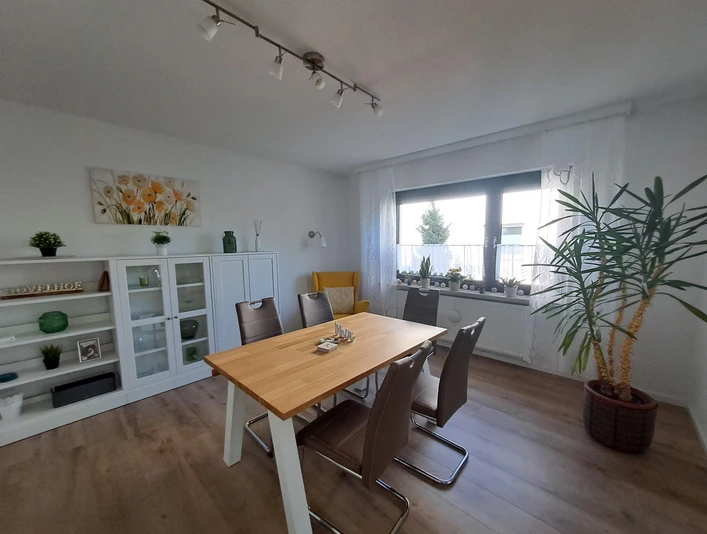 Ferienwohnung Berenbrinker (5).jpg Helles Wohnzimmer mit großem Esstisch, modernen Stühlen und Fenster zur Terrasse. Holzfußboden ergänzt.