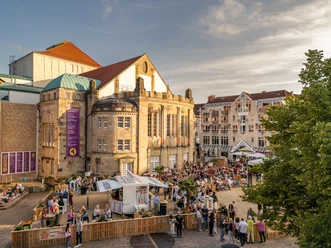 Theater Beach Osnabrück.jpg Historisches Theatergebäude im Abendlicht, umgeben von zahlreichen Besuchern, die ein Event genießen.
