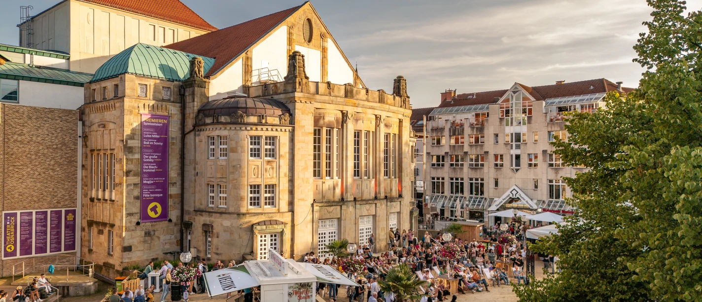 Theater Beach Osnabrück.jpg Historisches Theatergebäude im Abendlicht, umgeben von zahlreichen Besuchern, die ein Event genießen.