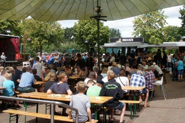 Zwischenberger Fest 3.jpg Eine lebhafte Menschenmenge genießt das Zwischenberger Fest, umgeben von Gastronomieständen und schattenspendenden Bäumen.