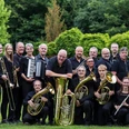 Blasorchester Bad Holzhausen Blasorchester in schwarzer Kleidung posiert mit verschiedenen Instrumenten in grüner, bewaldeter Umgebung.