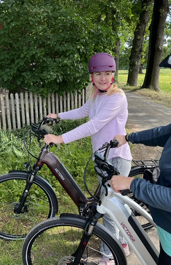Radfahren in der Mittelweser-Region Zwei Frauen mit Fahrradhelmen pausieren auf E-Bikes neben einem Feldweg, angrenzend an Bäume.