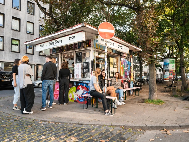 King Georg Kiosk Small kiosk in an urban setting, surrounded by trees and people in a relaxed atmosphere.