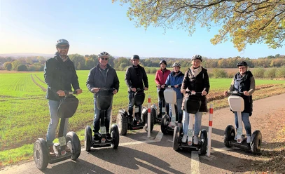 Tour Herford 1 (2)_.jpg Gruppe von Menschen auf Segways fährt bei sonnigem Wetter entlang eines Feldwegs, im Hintergrund Wälder.