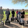 Tour Herford 1 (2)_.jpg Gruppe von Menschen auf Segways fährt bei sonnigem Wetter entlang eines Feldwegs, im Hintergrund Wälder.