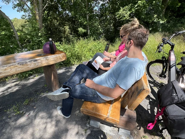 Radfahren in der Mittelweser-Region Ein Paar sitzt auf einer Holzbank in einem schattigen Park, neben ihnen stehen Fahrräder.