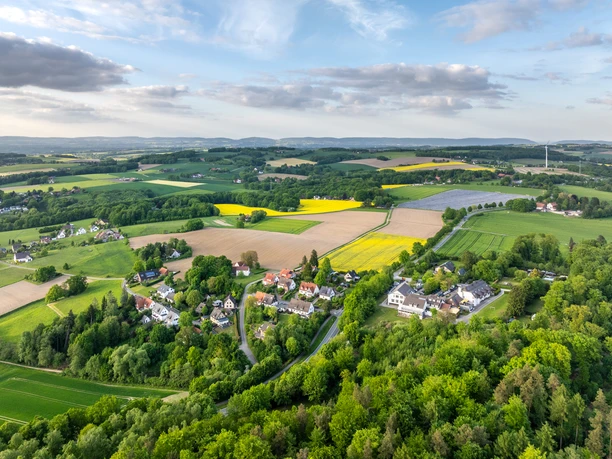 Ländliche Landschaft mit Feldern und kleinen Ansiedlungen unter blauem Himmel mit vereinzelten Wolken.