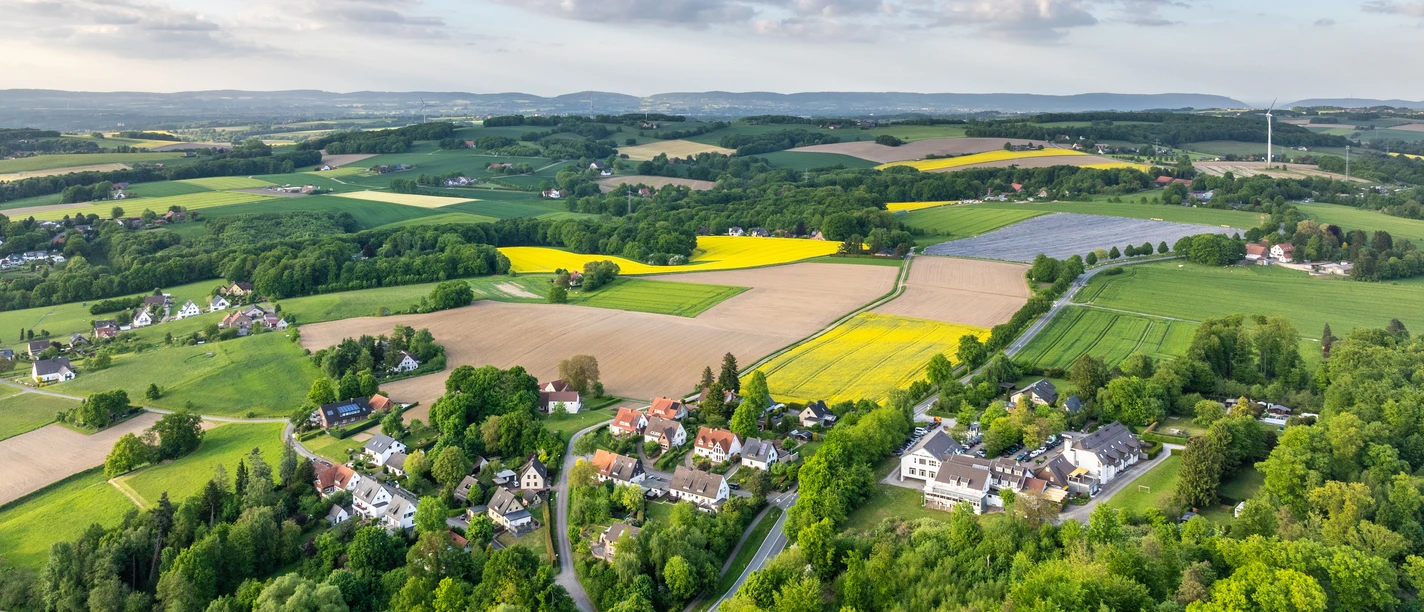 Herford-Bismarckturm-2025-005-©Teutoburger Wald - WfG Herford - D. Ketz.jpg Ländliche Landschaft mit Feldern und kleinen Ansiedlungen unter blauem Himmel mit vereinzelten Wolken.
