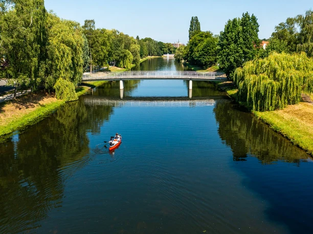 Ein rotes Kanu mit zwei Personen paddelt auf einem ruhigen Fluss unter einer modernen Brücke.