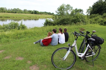 Four people enjoy the view of a river while two bicycles are parked on a meadow.