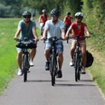 Eine Gruppe Radfahrer mit Helmen unterwegs auf einem asphaltierten Weg durch grüne Landschaft.