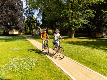 herford-promenade-teutoburger-wald-tourismus-h-tornow-015-jpg.jpg Zwei Personen fahren bei sonnigem Wetter auf Fahrrädern durch einen grünen Parkweg.