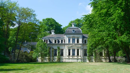 Aussenaufnahme des Palais Rastede Ein prächtiges Herrenhaus mit eleganter Architektur umrahmt von üppigem Grün in einem gepflegten Park.