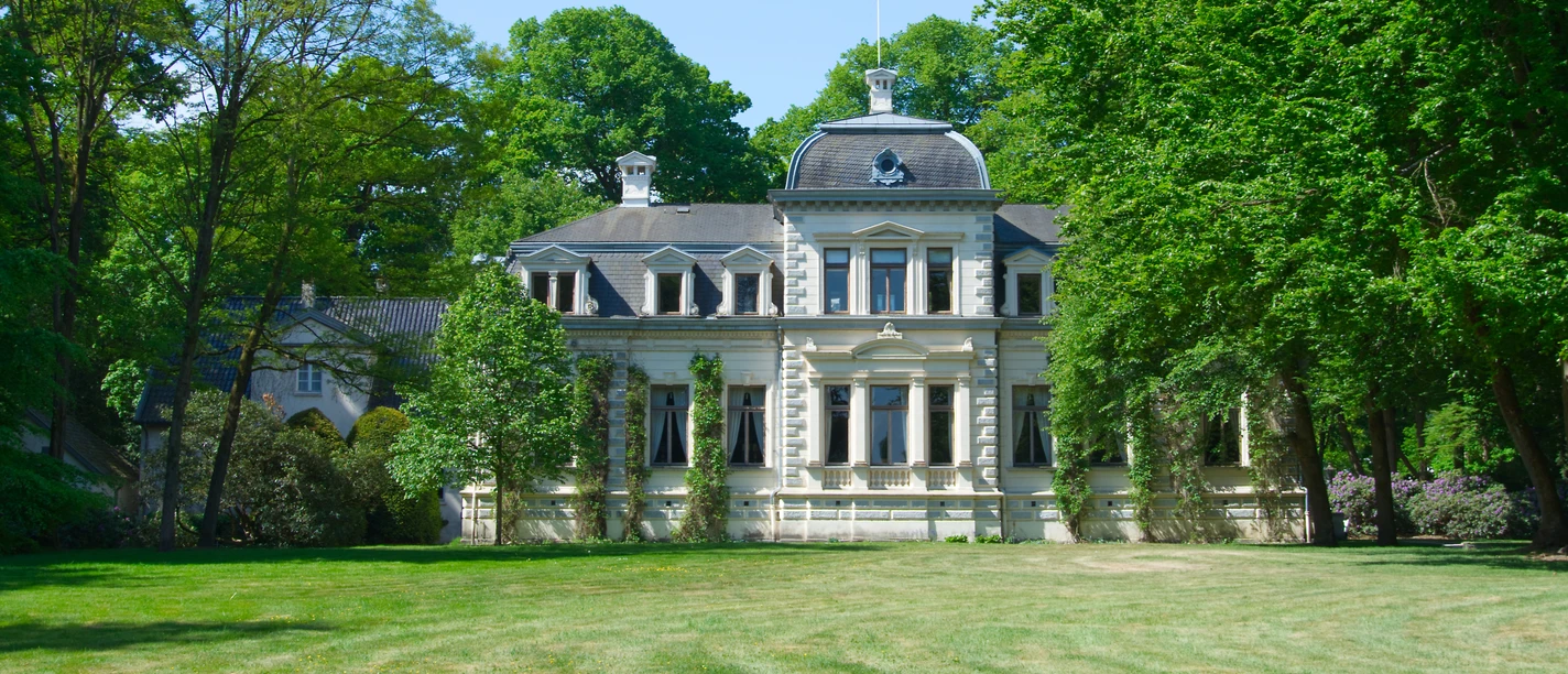 Aussenaufnahme des Palais Rastede Ein prächtiges Herrenhaus mit eleganter Architektur umrahmt von üppigem Grün in einem gepflegten Park.