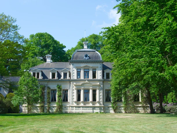 Ein prächtiges Herrenhaus mit eleganter Architektur umrahmt von üppigem Grün in einem gepflegten Park.