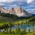 Dolomiten_Kal. SHS.jpg Ein malerischer Bergsee, umgeben von saftig grünen Wiesen und majestätischen Dolomiten, unter strahlend blauem Himmel.