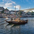 Portugal_Kal. SHS.jpg Das Bild zeigt traditionelle Boote im Fluss Douro vor der beeindruckenden Kulisse Portos. Im Hintergrund erhebt sich die ikonische Dom-Luís-I-Brücke vor einer üppigen Flusslandschaft.