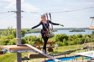 Kletterpark Markkleeberg - Freizeitaktivitäten in Leipzig und Region.jpg Eine junge Frau balanciert über einen Holzbalken im Kletterpark Markkleeberg, im Hintergrund ist der Markkleeberger See zu erkennen.