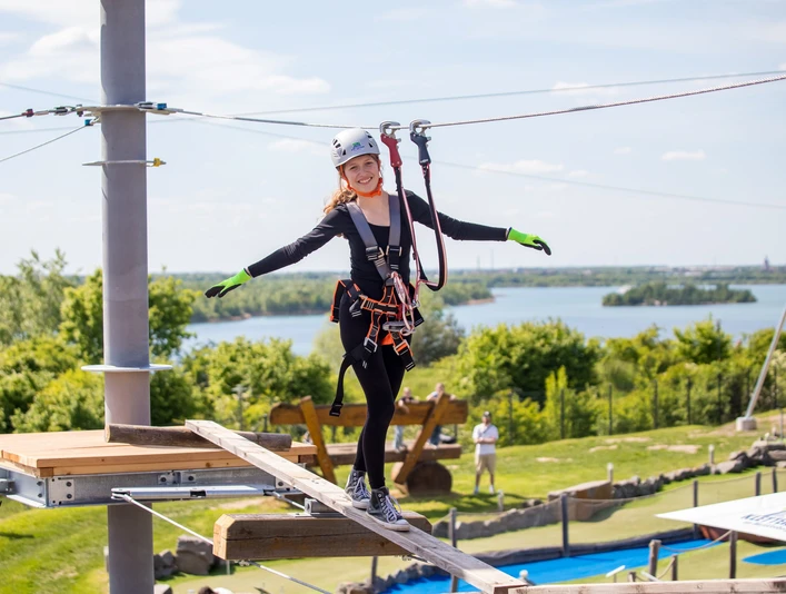 Kletterpark Markkleeberg - Freizeitaktivitäten in Leipzig und Region.jpg Eine junge Frau balanciert über einen Holzbalken im Kletterpark Markkleeberg, im Hintergrund ist der Markkleeberger See zu erkennen.