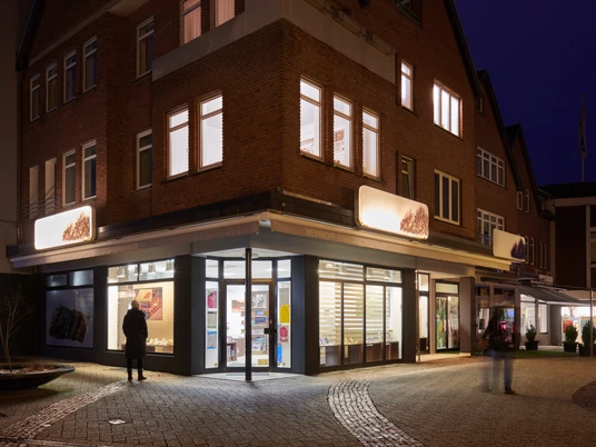 Das Bild zeigt ein beleuchtetes Geschäft in einer abendlichen Straßenszene am Gänsemarkt in Herford.