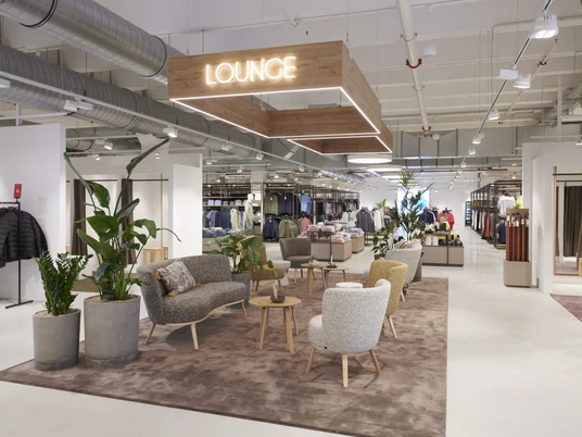 Ein modernes Modegeschäft mit einer komfortablen Lounge, umgeben von Pflanzen und eleganter Dekoration.