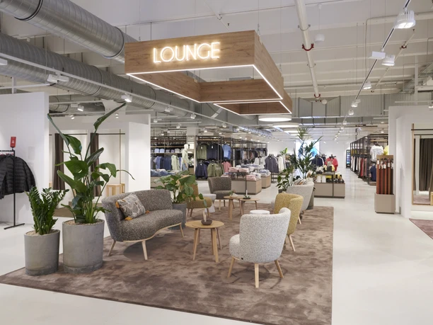 Ein modernes Modegeschäft mit einer komfortablen Lounge, umgeben von Pflanzen und eleganter Dekoration.