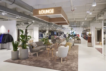 BRAX Outlet Herford-Leineweber GmbH & Co KG(5).jpg Ein modernes Modegeschäft mit einer komfortablen Lounge, umgeben von Pflanzen und eleganter Dekoration.