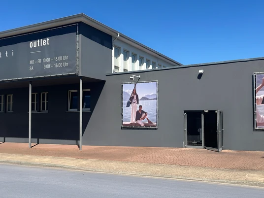 Grauer Gebäudekomplex mit großen Werbepostern und Bugatti-Schriftzug, klare Linien und moderne Architektur.