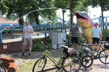 People enjoying a sunny day in a park, surrounded by bicycles and a large, colorful sculpture.