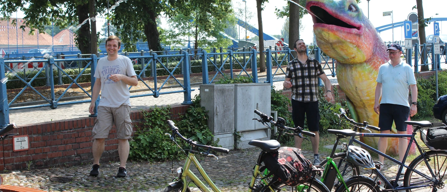 Radfahren in der Mittelweser-Region People enjoying a sunny day in a park, surrounded by bicycles and a large, colorful sculpture.