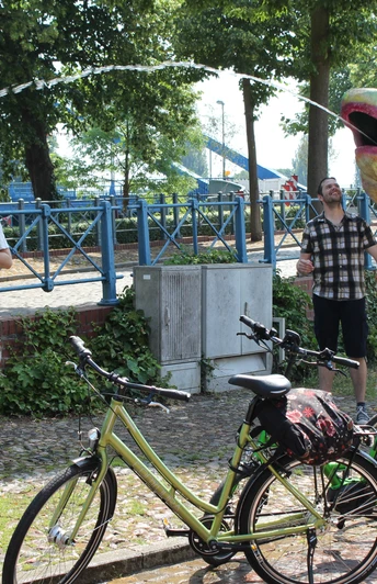 Radfahren in der Mittelweser-Region Menschen genießen einen sonnigen Tag in einem Park, umgeben von Fahrrädern und einer großen, bunten Skulptur.