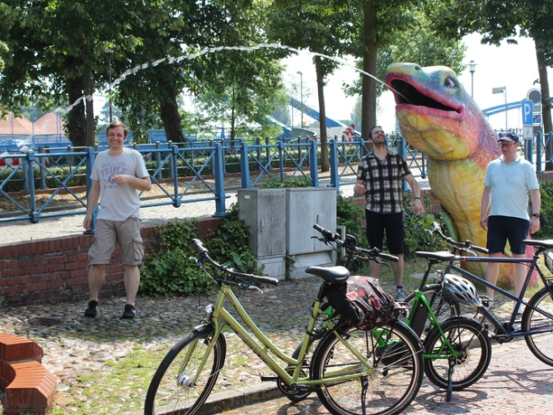 Radfahren in der Mittelweser-Region Menschen genießen einen sonnigen Tag in einem Park, umgeben von Fahrrädern und einer großen, bunten Skulptur.