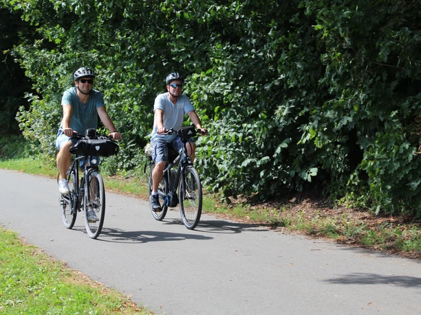 Two cyclists on a path surrounded by lush greenery, enjoying a relaxing ride in the countryside.