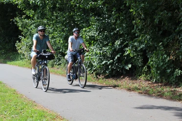 Ueberlandtour Zwei Radfahrer auf einem Weg, umgeben von üppigem Grün, genießen eine entspannte Fahrt in der Natur.