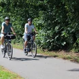 Ueberlandtour Zwei Radfahrer auf einem Weg, umgeben von üppigem Grün, genießen eine entspannte Fahrt in der Natur.
