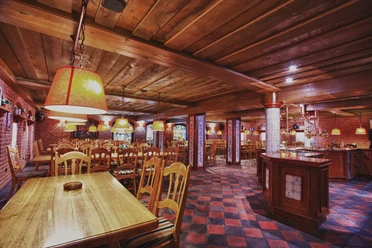 Bierreise - Herforder Brauerei.jpg Ein rustikaler Raum mit Holztischen, Stühlen und warmen Beleuchtung für gesellige Brauereirunden.
