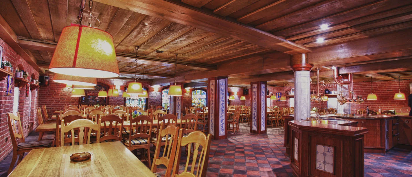 Bierreise - Herforder Brauerei.jpg Ein rustikaler Raum mit Holztischen, Stühlen und warmen Beleuchtung für gesellige Brauereirunden.