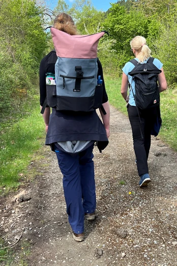 Zwei Wanderer mit Rucksäcken gehen einen naturbelassenen Weg in der grünen Mittelweser-Region entlang.