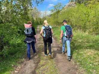 Drie mensen lopen over een natuurlijk pad, omringd door fris groen en een blauwe lucht.